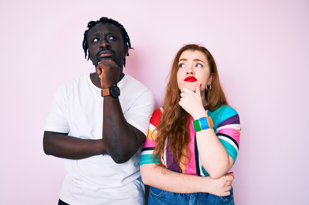Interracial couple wearing casual clothes with hand on chin thinking about question, pensive expression. smiling with thoughtful face. doubt concept.  - Photo, Image