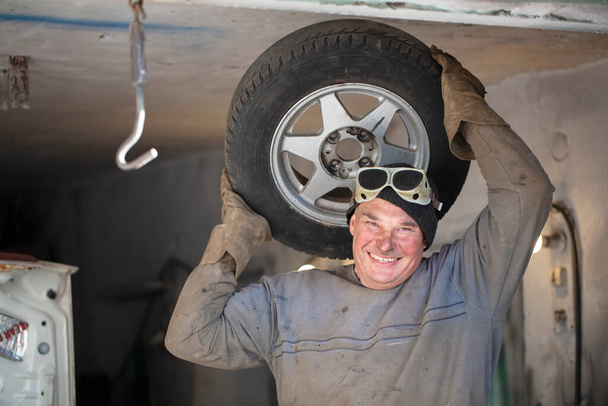 Otomobil tamircisi, araba tekerli bir garajda. Lastiklere uyuyor. - Fotoğraf, Görsel