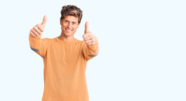 Young handsome man wearing casual clothes approving doing positive gesture with hand, thumbs up smiling and happy for success. winner gesture.  - Photo, Image