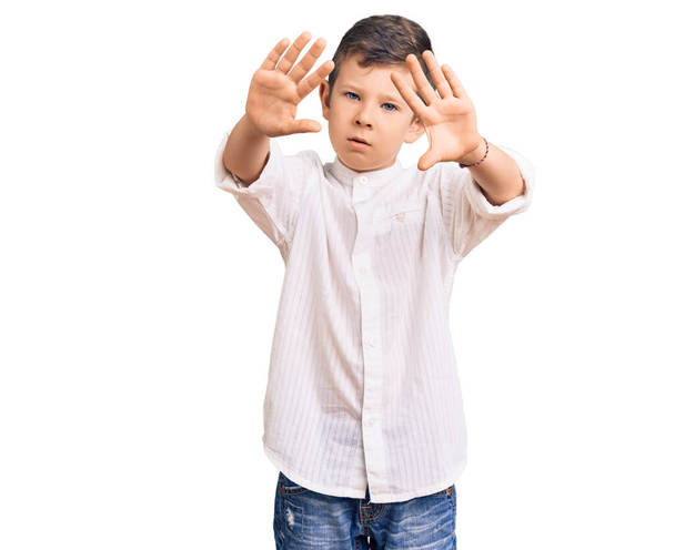 Lindo niño rubio con camisa elegante haciendo marco usando manos palmas y dedos, perspectiva de la cámara  - Foto, Imagen