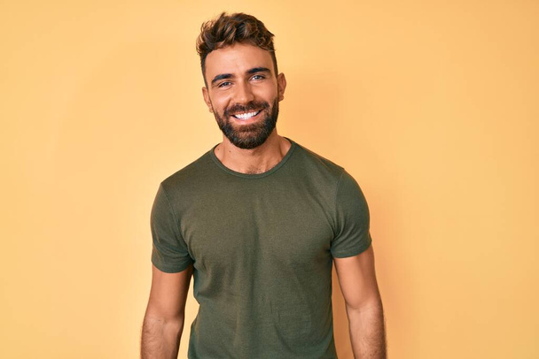 Junger hispanischer Mann in lässiger Kleidung, der im Stehen positiv und glücklich aussieht und mit einem selbstbewussten Lächeln lächelt, das Zähne zeigt  - Foto, Bild