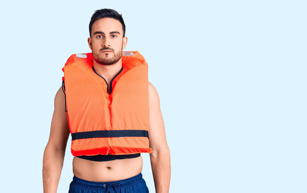 Young handsome man wearing lifejacket with serious expression on face. simple and natural looking at the camera.  - Photo, Image