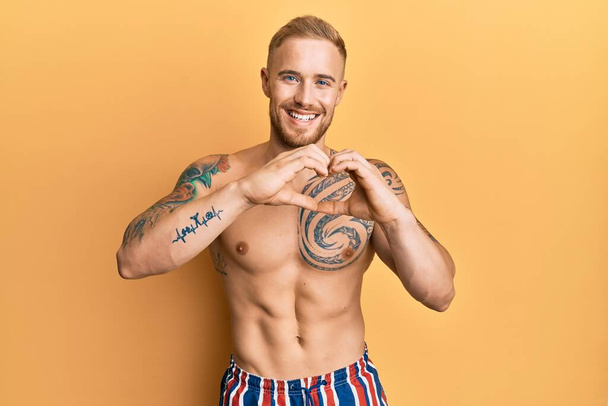 Young caucasian man wearing swimwear shirtless smiling in love doing heart symbol shape with hands. romantic concept.  - Photo, Image