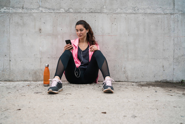 Portret atletycznej kobiety używającej telefonu komórkowego w przerwie od treningu na szarym tle. Sport i zdrowie Styl życia. - Zdjęcie, obraz
