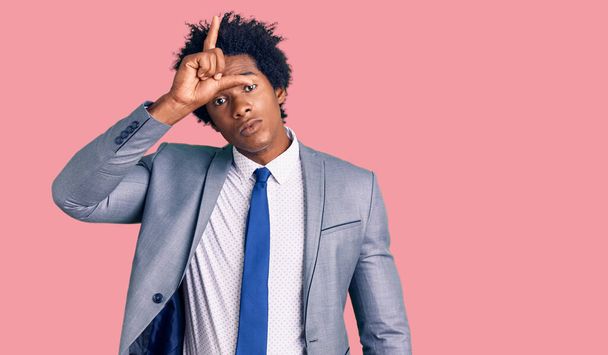 Handsome african american man with afro hair wearing business jacket making fun of people with fingers on forehead doing loser gesture mocking and insulting.  - Photo, Image