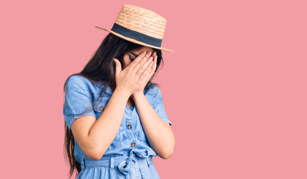 Brunette teenager girl wearing summer hat with sad expression covering face with hands while crying. depression concept.  - Photo, Image