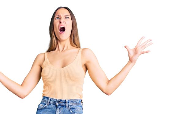 Beautiful brunette young woman wearing casual clothes crazy and mad shouting and yelling with aggressive expression and arms raised. frustration concept.  - Photo, Image