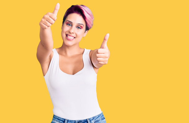 Young beautiful woman with pink hair wearing casual clothes approving doing positive gesture with hand, thumbs up smiling and happy for success. winner gesture.  - Photo, Image