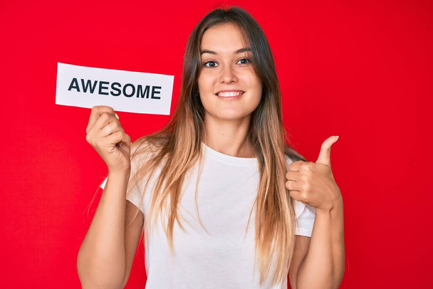 Beautiful caucasian woman holding awesome banner smiling happy and positive, thumb up doing excellent and approval sign  - Foto, Bild