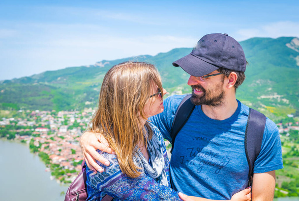 Detailní záběr na mladý pár objímající se navzájem a usmívá tváří v tvář s panoramatickým výhledem na zelenou přírodu a město Mtkheta v Gruzii. Vztah kamarádů na cestách. koncept cestování páry radost - Fotografie, Obrázek