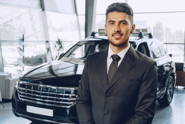 Friendly handsome car seller man standing in car salon - Photo, Image
