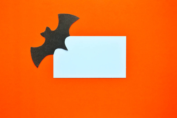 Black paper bat lies on orange background with white mockup - Fotografie, Obrázek
