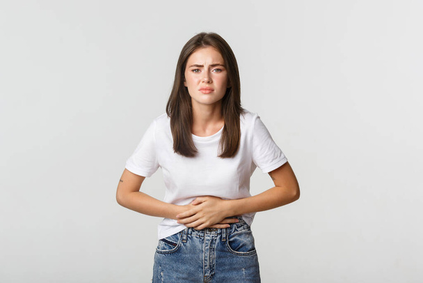 Woman having stomach ache, bending and holding hands on belly, discomfort from menstrual cramps. Girl feeling nauseous - Fotó, kép