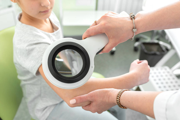 A dermatologist examines a teenagers skin condition with a dermatoscope. - 写真・画像
