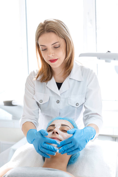 Woman professional doctor beautician applies a mask on a patient's face for skin care. Cosmetic procedures for skin rejuvenation and nutrition. - Foto, Bild