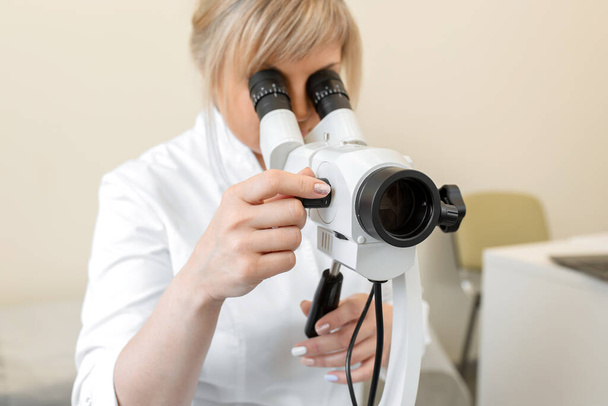 Female blond doctor gynecologist looks through a colposcope. Examination by a gynecologist. Female health concept. - Foto, imagen