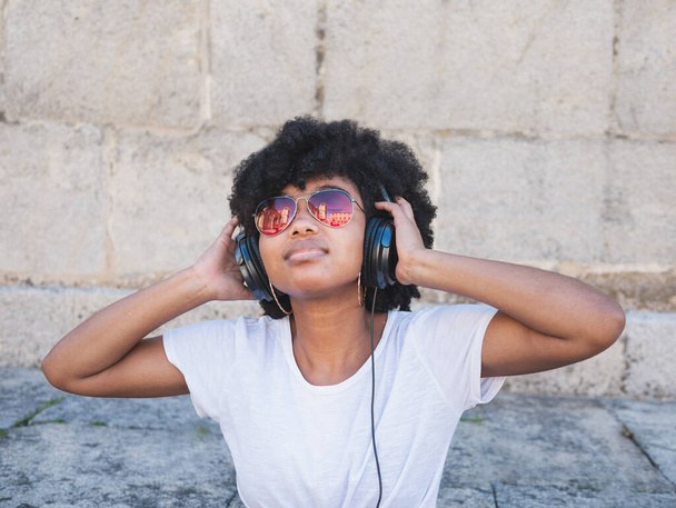 Чернокожая девушка, слушающая музыку в наушниках, на улице, изолирована - Фото, изображение