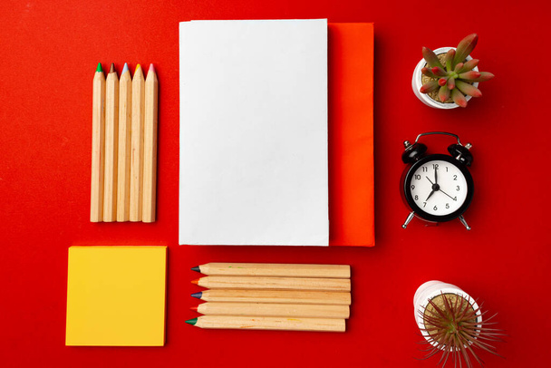 Open notepad with color pencils and flower pots on red background - Photo, Image