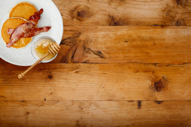A plate of bacon and pancakes, drizzled with honey on a rustic wooden background with space for copy - Foto, Imagem