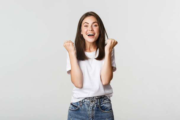 Веселая привлекательная брюнетка девушка кулаком насос и улыбаясь от радости, выигрывая - Фото, изображение