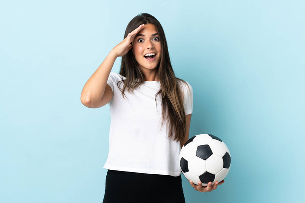 Young football player brazilian girl isolated on blue background with surprise expression - Фото, изображение