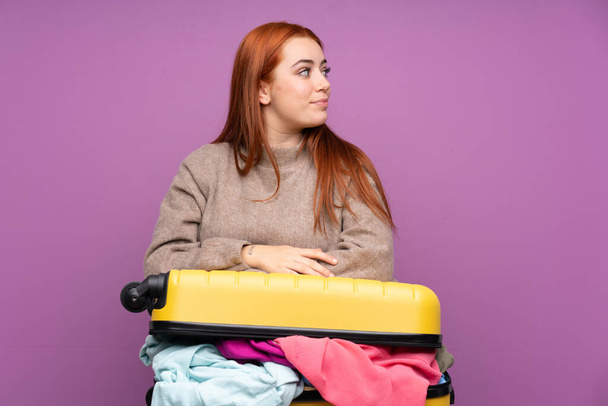 Reisender Teenager mit einem Koffer voller Kleider, der zur Seite schaut - Foto, Bild