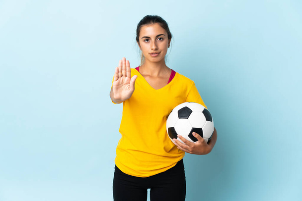 Молодая испаноязычная футболистка в изоляции на синем фоне делает жест остановки - Фото, изображение