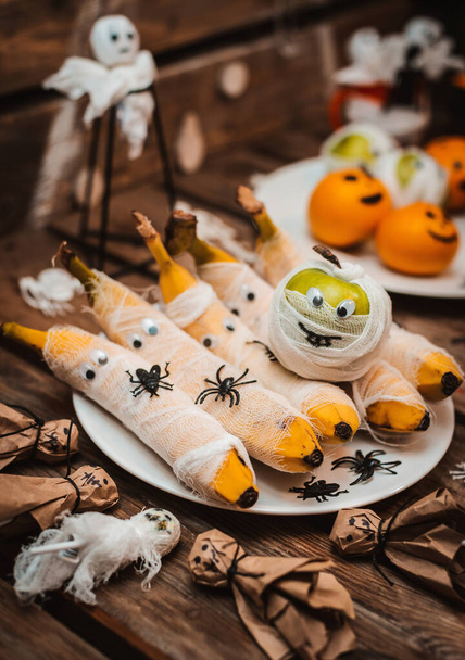 Sweet table with fruits and treats for Halloween. Decorations Apple bananas in the form of a mummy with eyes and a Ghost. spiders and cockroaches - Photo, Image