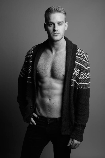 Studio shot of young handsome man shirtless under cardigan sweater against gray background in black and white - Photo, Image