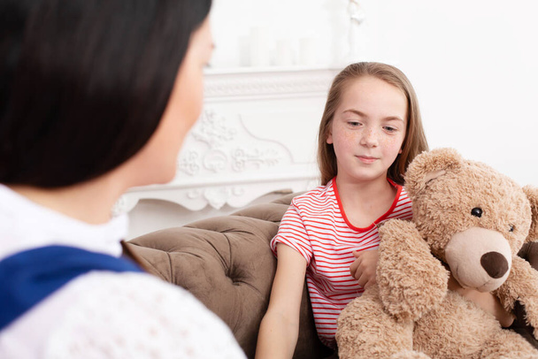 Teen girl on reception at the psychotherapist. Psychotherapy session for children. The psychologist works with the patient. Girl smiling sitting on a sofa next to a sitting female doctor therapist. - Fotografie, Obrázek