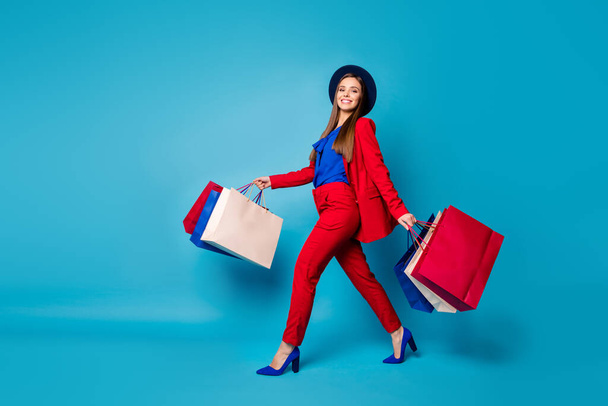 Full body profile photo of confident lady boss walk shopping center hold many packs wear retro cap red suit shirt blazer pants high-heels isolated blue color background - Fotografie, Obrázek
