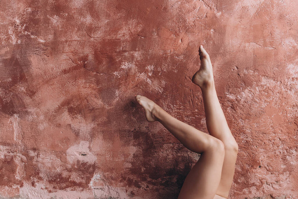 elegant female legs. A young girl performs gymnastic exercises by lifting her tanned beautiful legs up and leaning them against the wall - Foto, Imagen