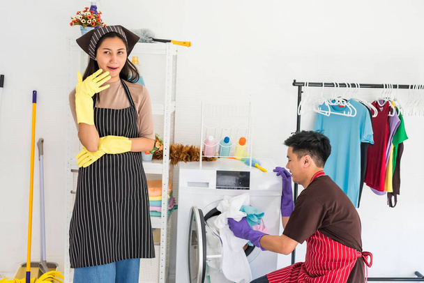 アジアの若いアイドル主婦は、自分で洗濯する夫やボーイフレンドを見て笑っています。怠惰な笑顔の妻は彼の仕事を制御しながら、男に家事. - 写真・画像