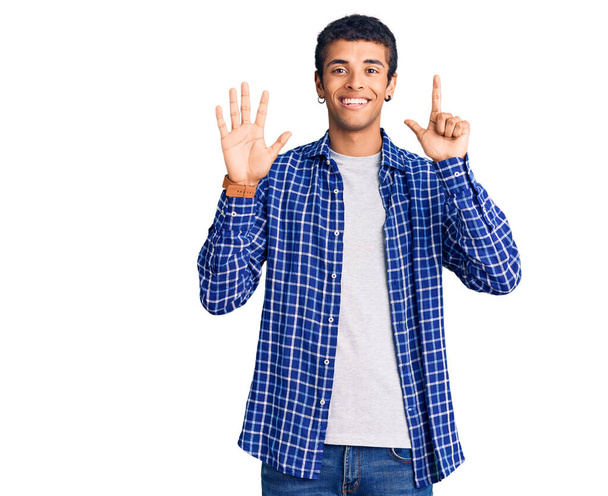 自信を持って幸せな笑みを浮かべている間、若いアフリカ系アメリカ人の男性は、カジュアルな服を着て指の数7を示すと指摘.  - 写真・画像