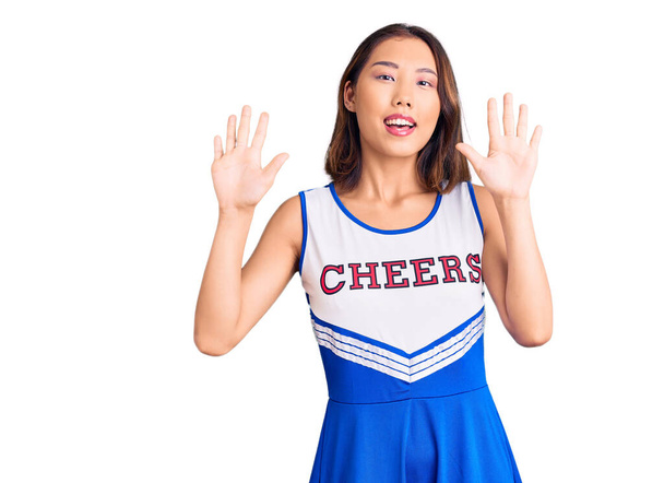 Nuori kaunis kiinalainen tyttö yllään cheerleader yhtenäinen osoittaa ja osoittaa ylös sormilla numero kymmenen hymyillen itsevarma ja onnellinen.  - Valokuva, kuva