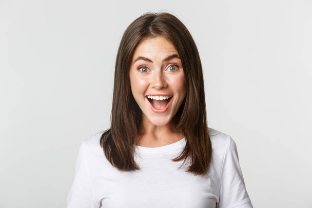 Portrait of joyful pretty brunette girl looking amused, smiling excited and surprised over white background - Foto, Imagem