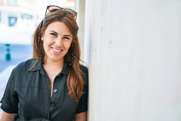 Молода іспаномовна жінка посміхається щасливим нахилившись на стіну на вулиці міста
 - Фото, зображення