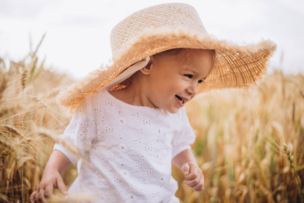 pretty cute baby girl with a beautiful smile wearing summer straw hat in a walk in the  wheat fields. selective focus. family, people concept - Fotografie, Obrázek