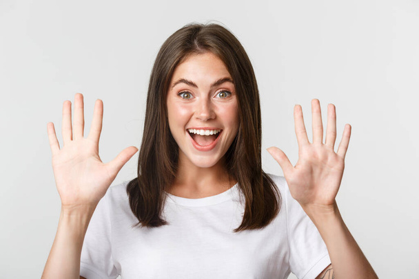 Primo piano di allegra giovane donna attraente sorridente, mostrando dieci dita, sfondo bianco - Foto, immagini