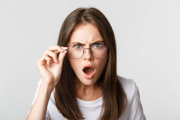 Close-up of insulted and shocked young angry woman looking from under glasses - Photo, Image