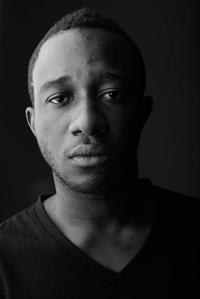 Studio shot of young African man in dark room against black background in black and white - Foto, Imagem
