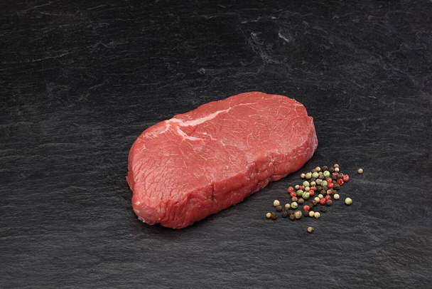 Hovězí steak na černé břidlicové desce s barevným pepřem. - Fotografie, Obrázek