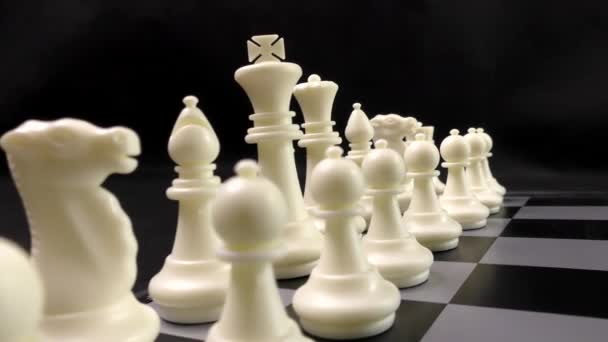 Joukkue mustia ja valkoisia shakkinappuloita. Shakkia shakkilaudalla. Tämä on älyllistä peliä. Musta tausta. - Materiaali, video