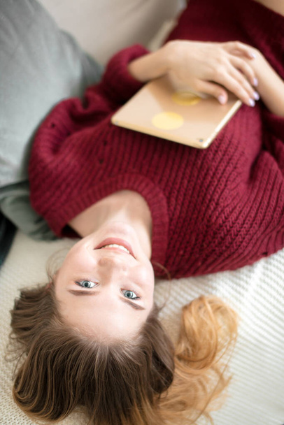 attractive woman with beautiful blue eyes lying on sofa and hugging tablet - Foto, afbeelding
