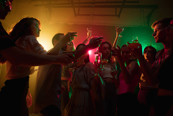 A crowd of people in silhouette raises their hands on dancefloor on neon light background - Fotó, kép