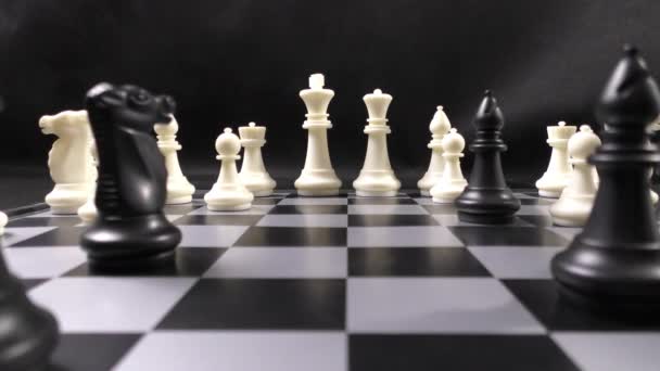 Egy csapat fekete-fehér sakkbábu. Sakk a sakktáblán. Ez intellektuális játék. Fekete háttér. - Felvétel, videó