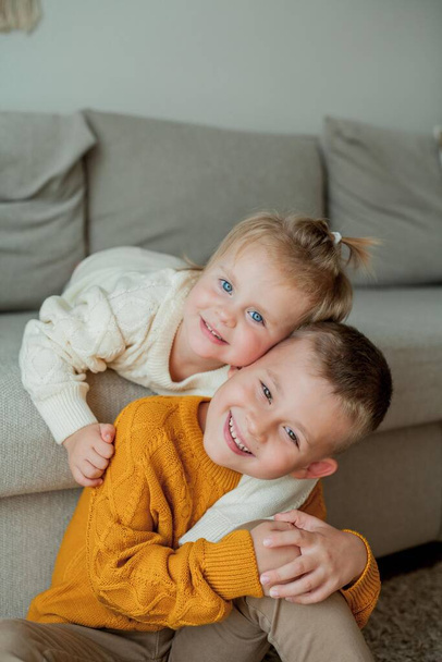 Little brother and sister in cozy knitted sweaters play at home. Portrait of cute little brother and sister. - Foto, imagen