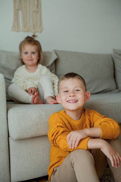 Little brother and sister in cozy knitted sweaters play at home. Portrait of cute little brother and sister. - Fotografie, Obrázek