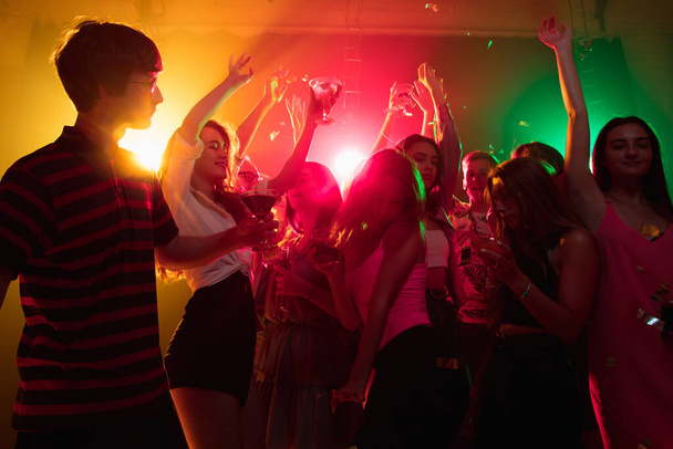 A crowd of people in silhouette raises their hands on dancefloor on neon light background - Photo, image