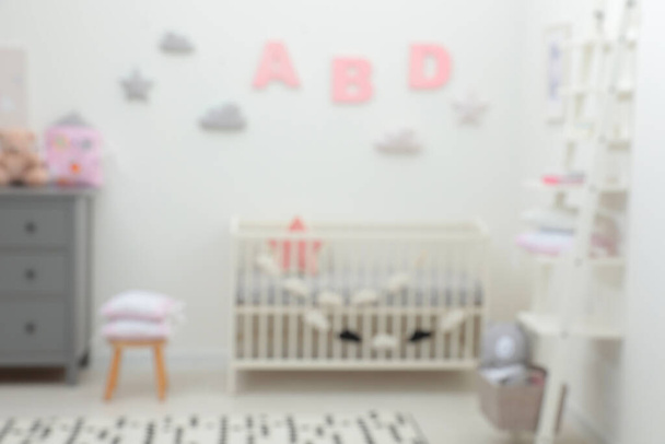 Blurred view of cute baby room interior with modern crib near white wall - Valokuva, kuva